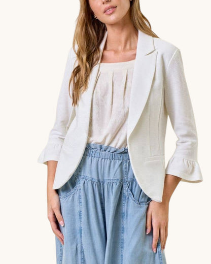 Woman wearing a white blazer over a white top with light blue jeans on a white background.
