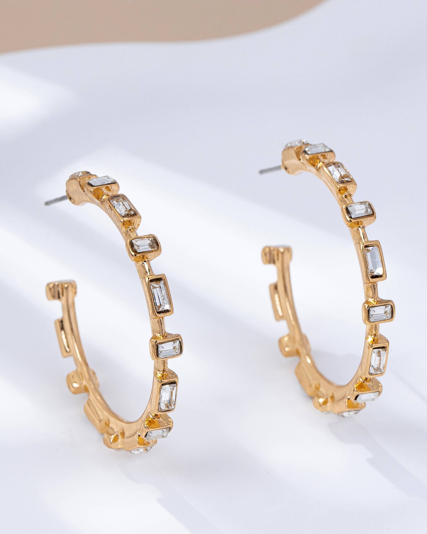 Gold hoop earrings with clear gemstones on a white surface.