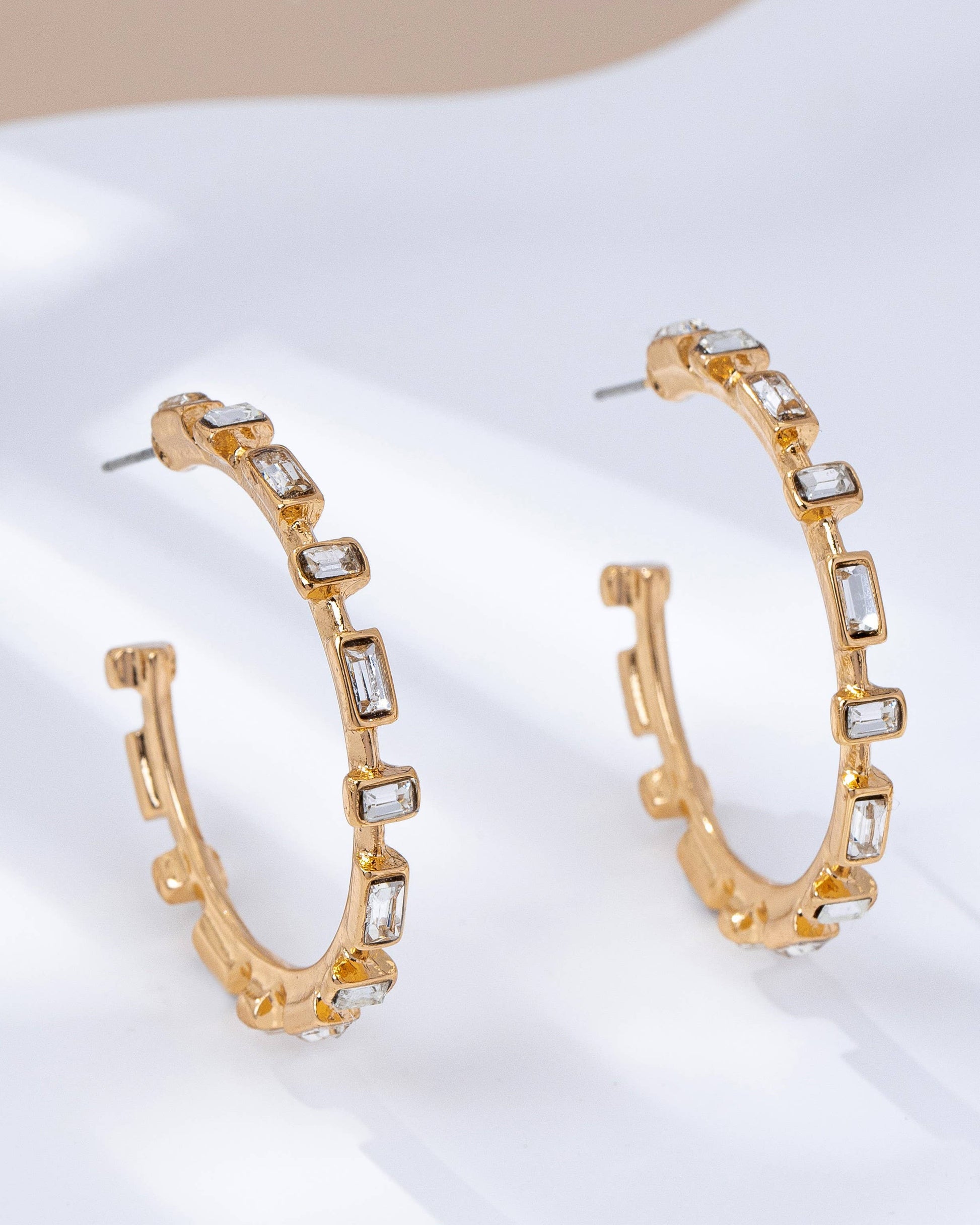 Gold hoop earrings with clear gemstones on a white surface.