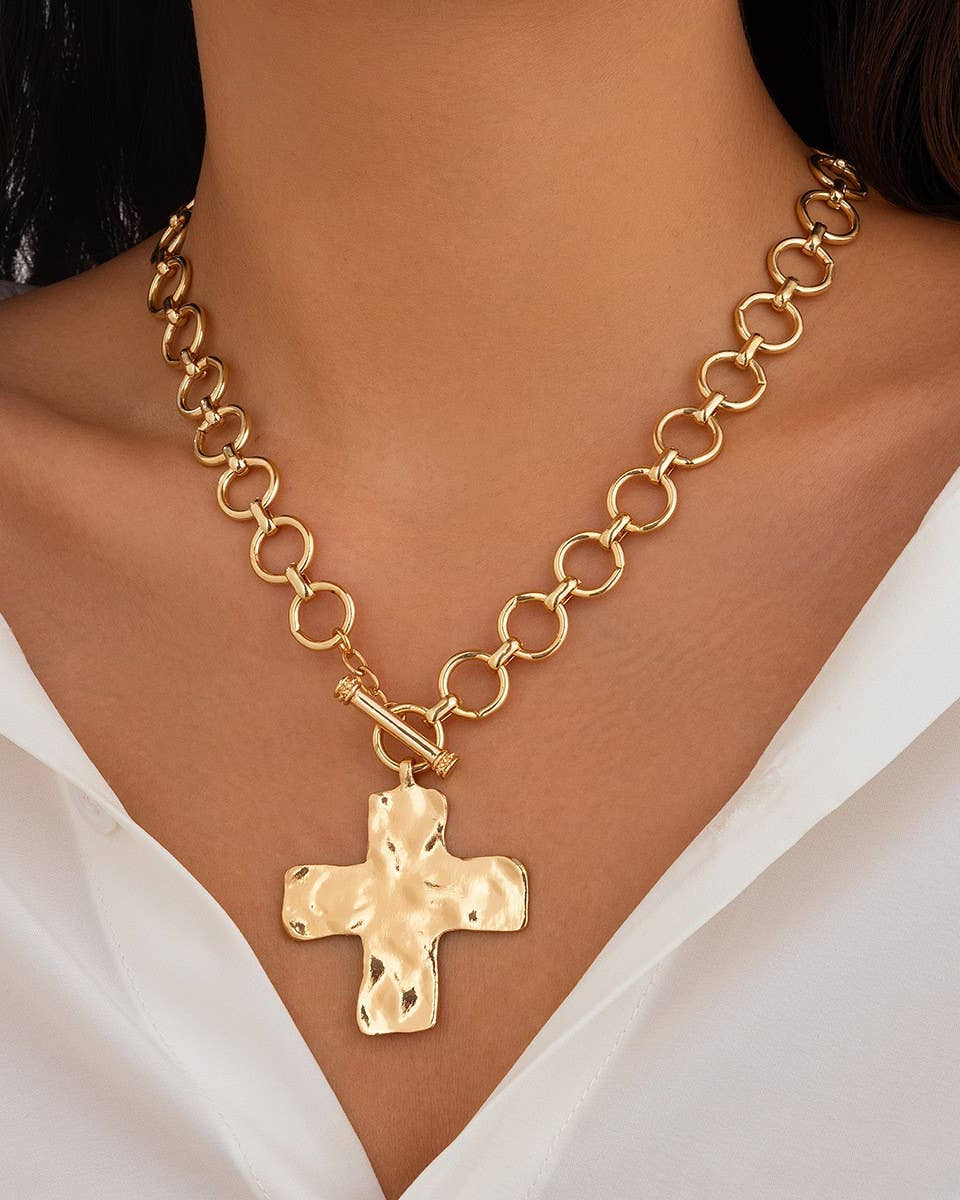 Gold chain necklace with a cross pendant on a person wearing a white top.