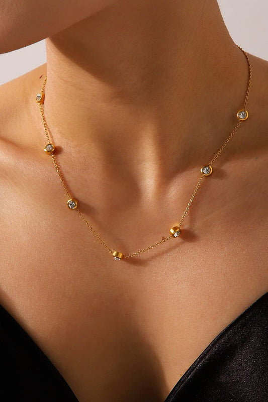 Gold necklace with small rhinestones on a person's neck against a neutral background.