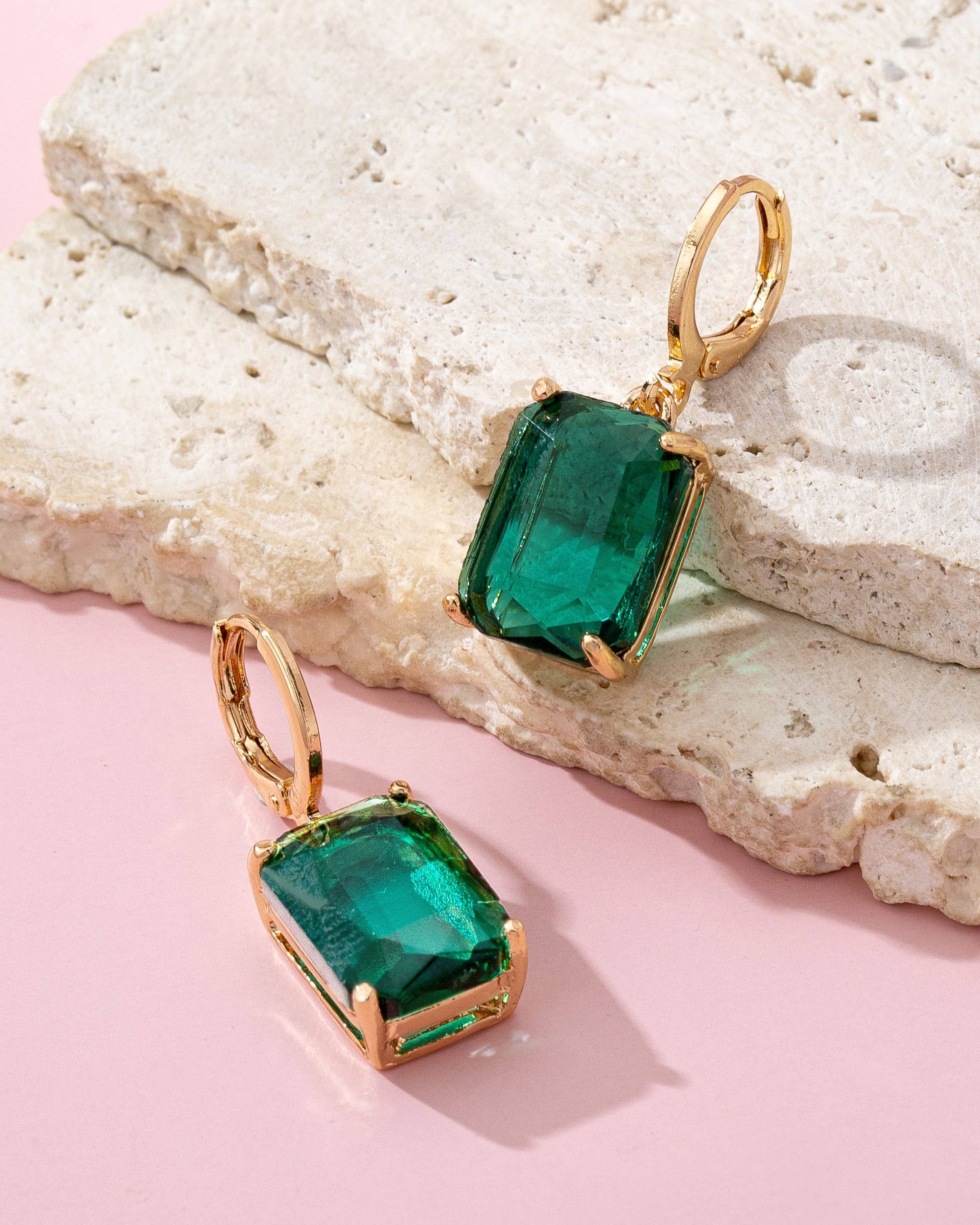 Green gemstone earrings with gold hooks on a textured stone surface.