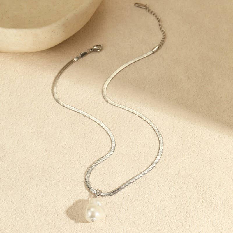Silver necklace with a pearl pendant on a beige surface.