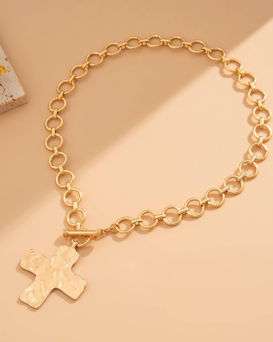 Gold chain necklace with a cross pendant on a beige background.