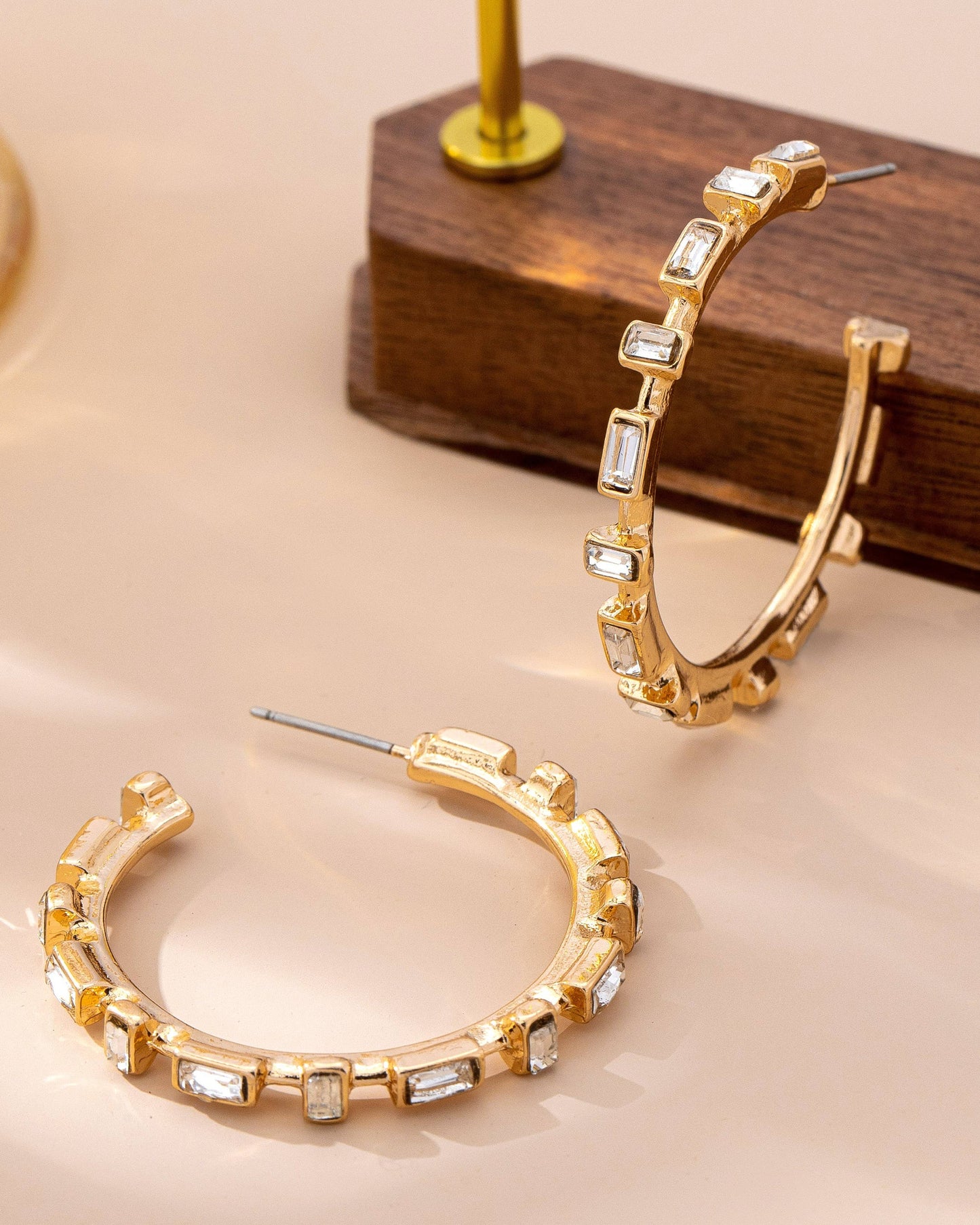 Gold hoop earrings with embedded stones on a beige surface.