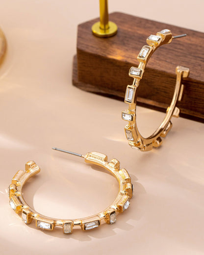 Gold hoop earrings with embedded stones on a beige surface.