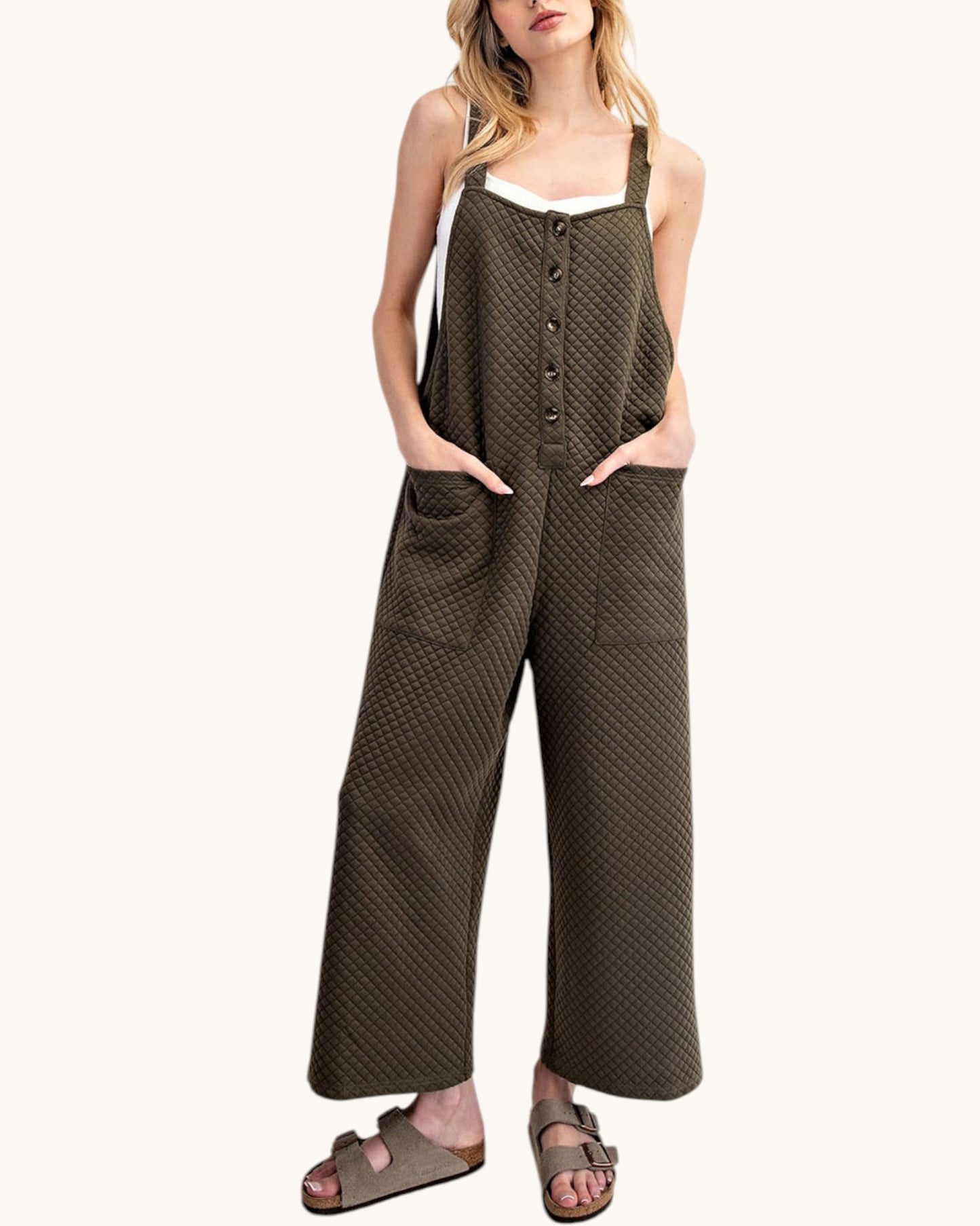 Woman wearing a dark green patterned sleeveless jumpsuit on a white background.