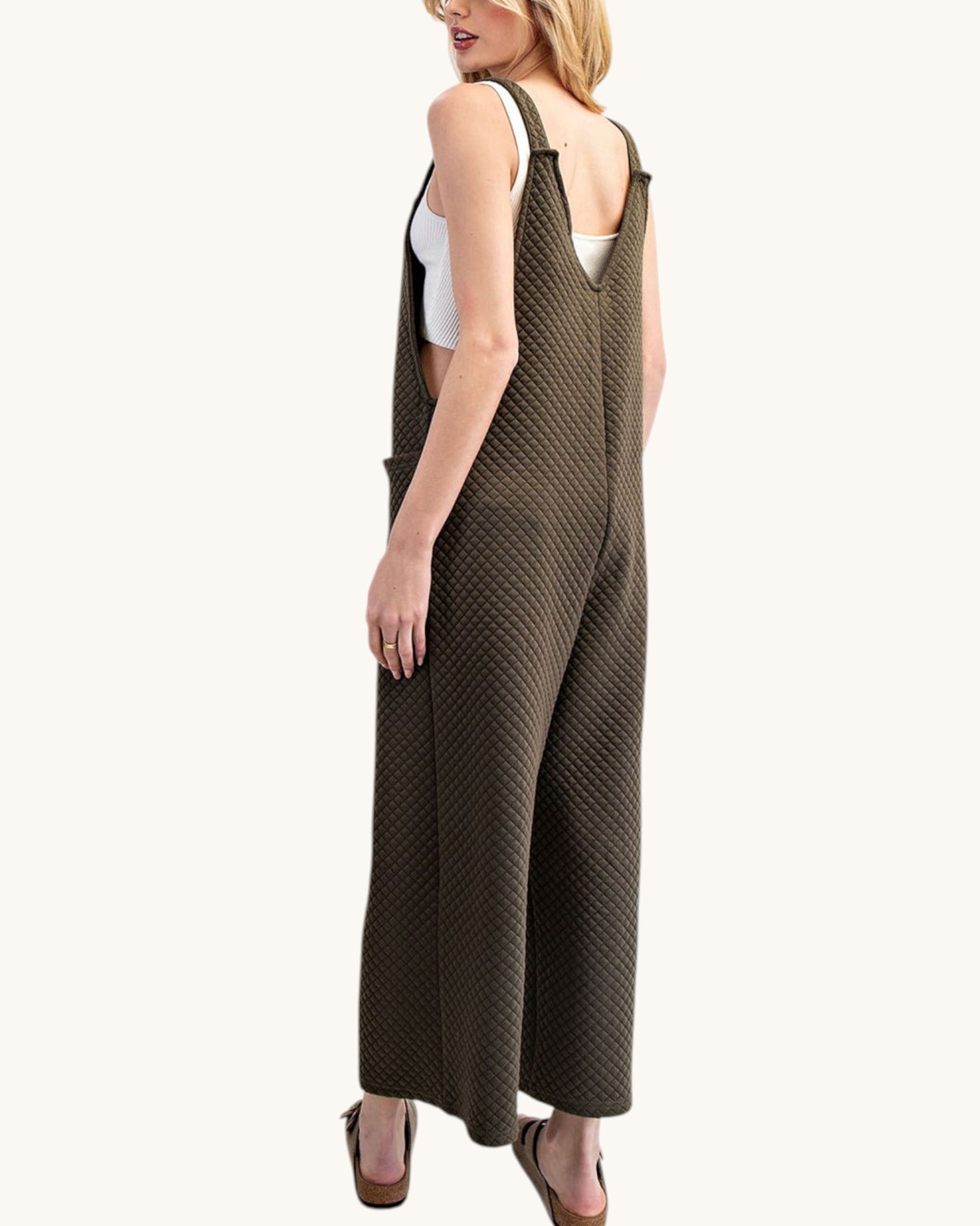 Woman wearing a moss colored sleeveless textured jumpsuit on a white background.