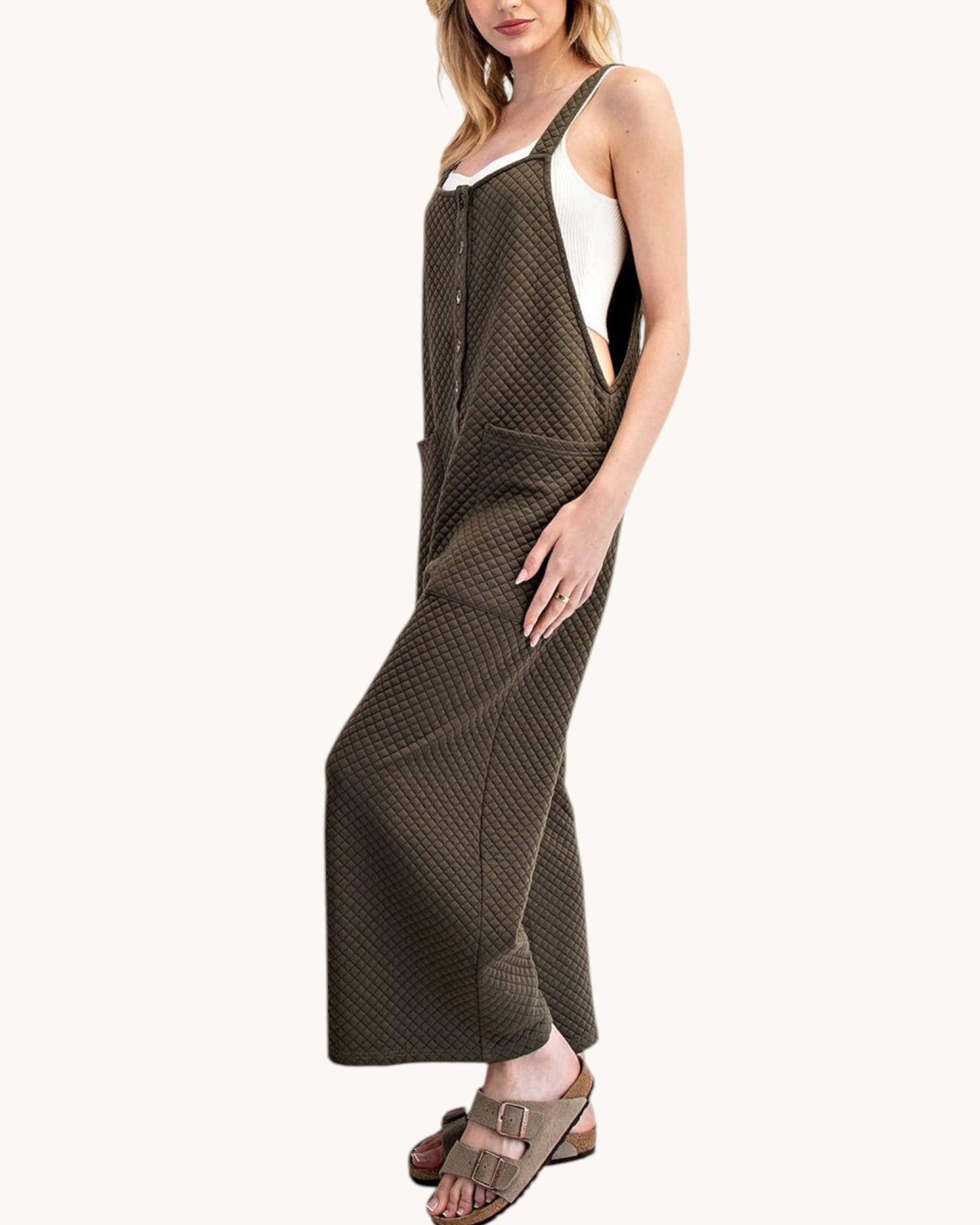 Woman wearing a moss colored sleeveless textured jumpsuit on a white background.