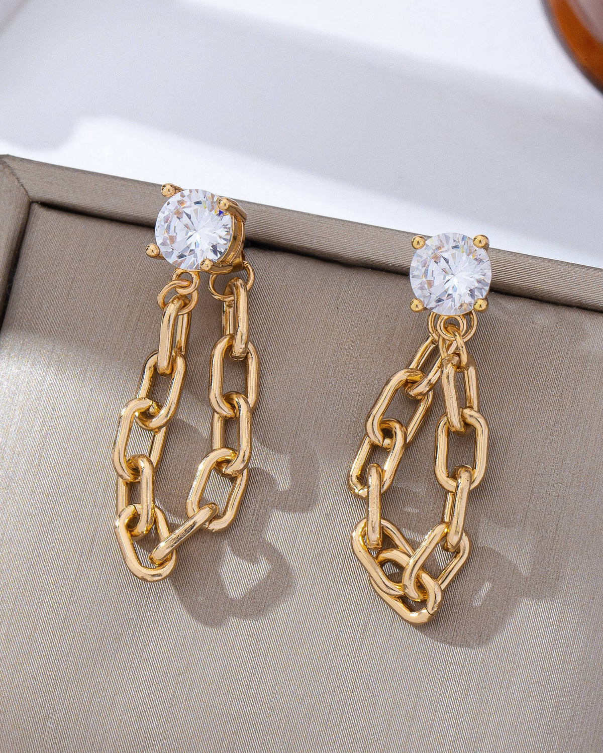 Gold chain earrings with clear gemstones on a beige fabric .background
