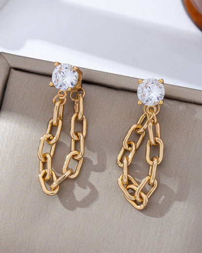 Gold chain earrings with clear gemstones on a beige fabric .background