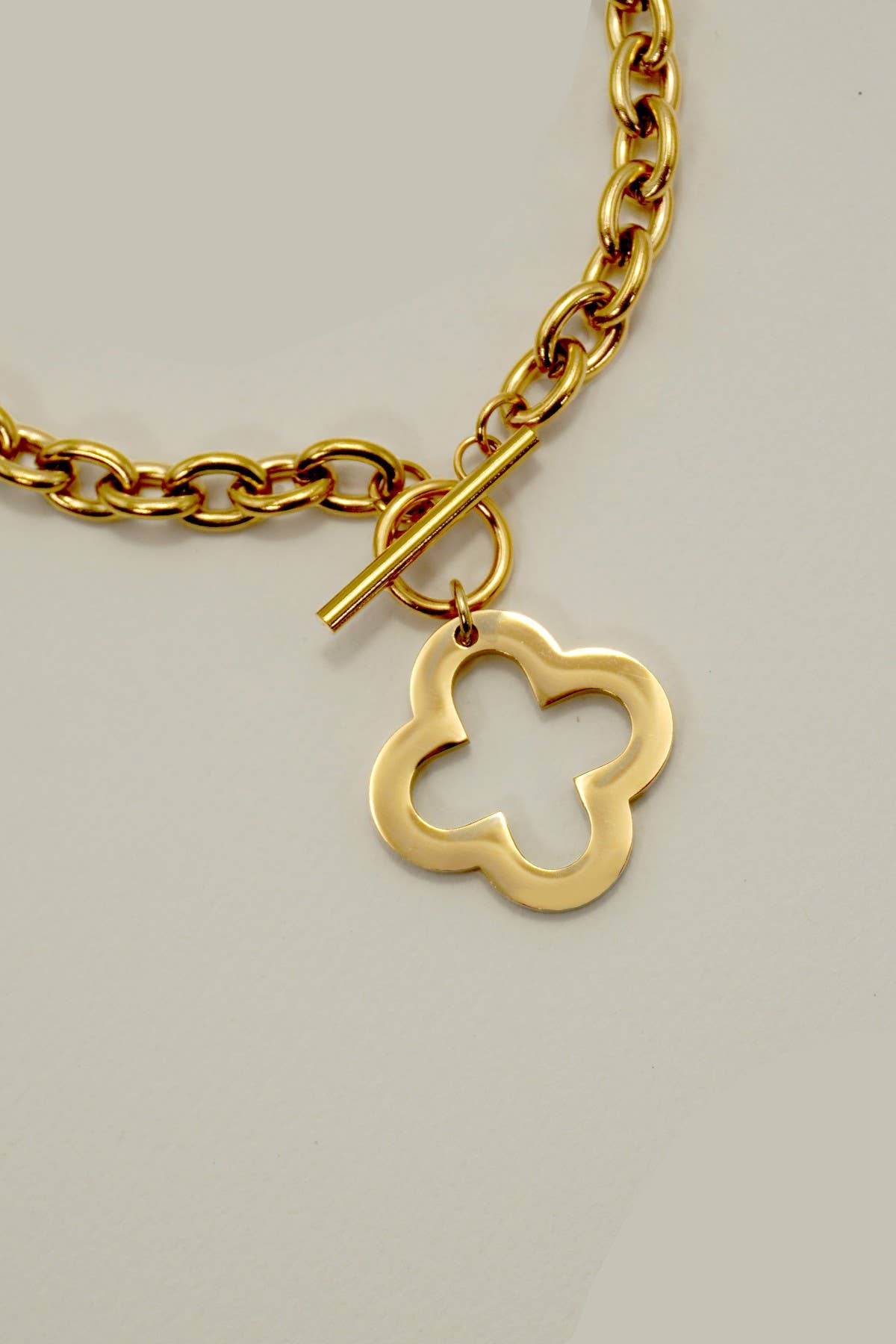 Gold chain necklace with a clover-shaped charm on a light gray background.