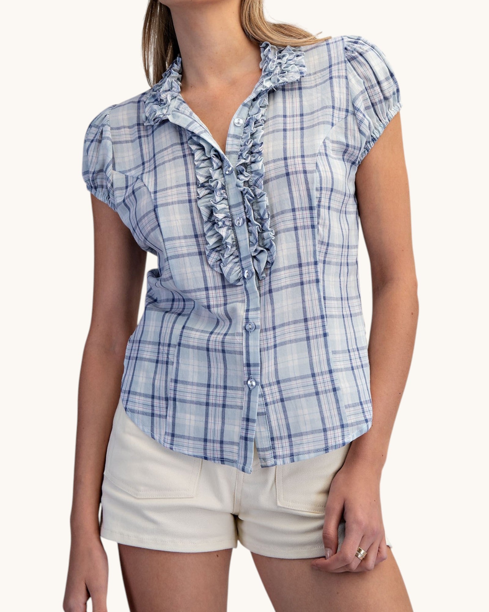 Woman wearing a blue plaid shirt with ruffles on a white background.