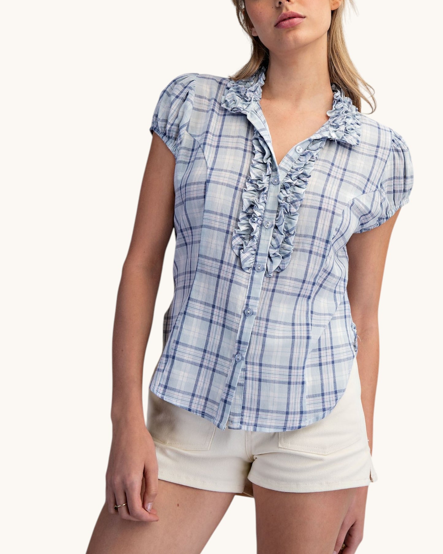 Woman wearing a blue plaid shirt with ruffle details on a white background.