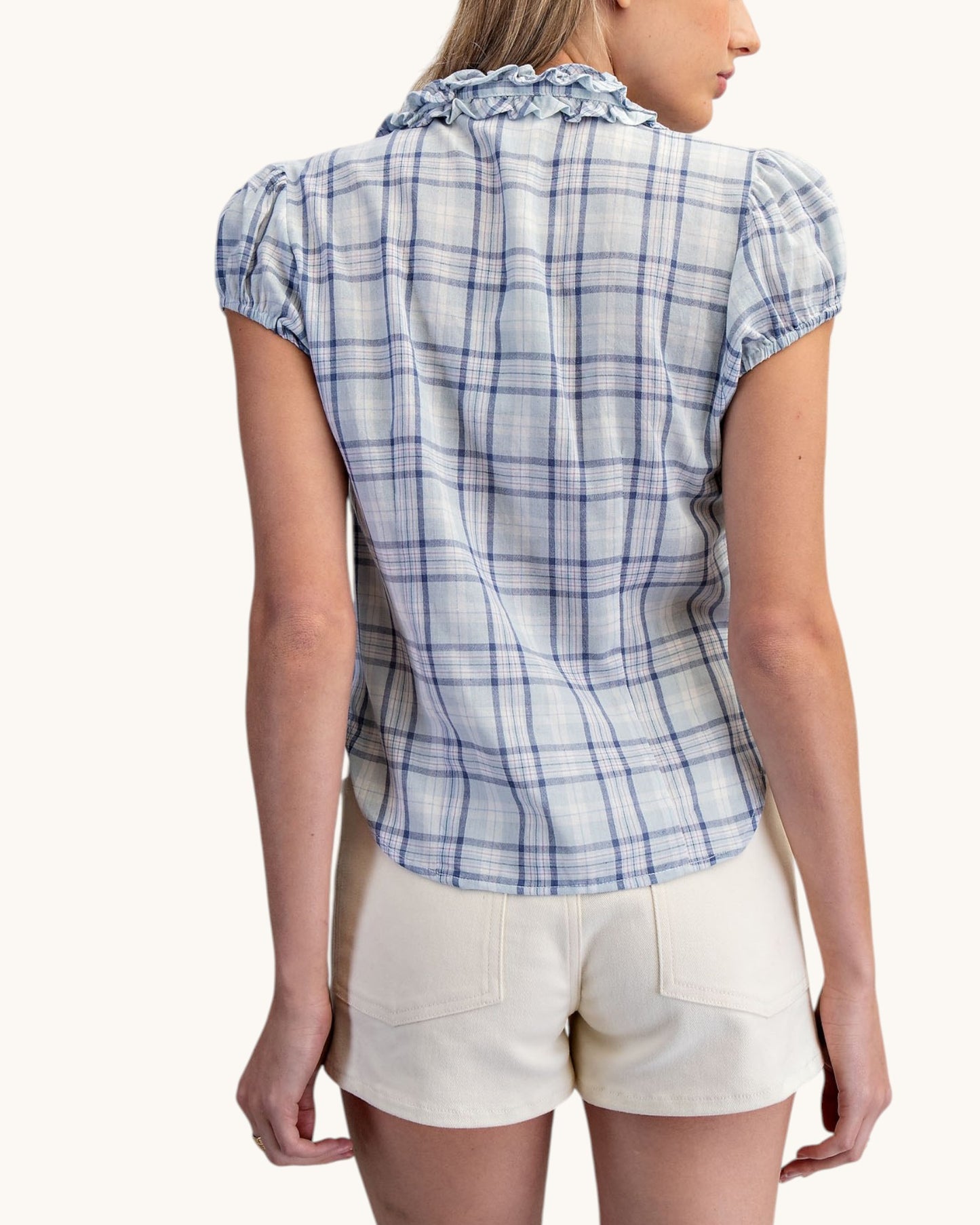Woman wearing a blue plaid shirt and white shorts on a white background.