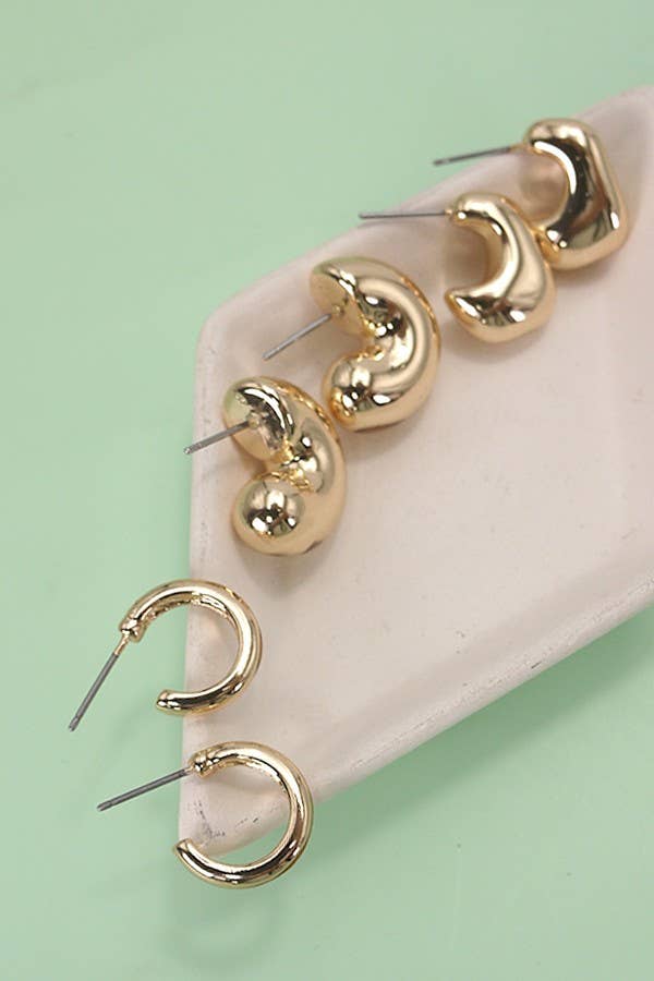Gold hoop earrings set on a beige stand against a light green background.