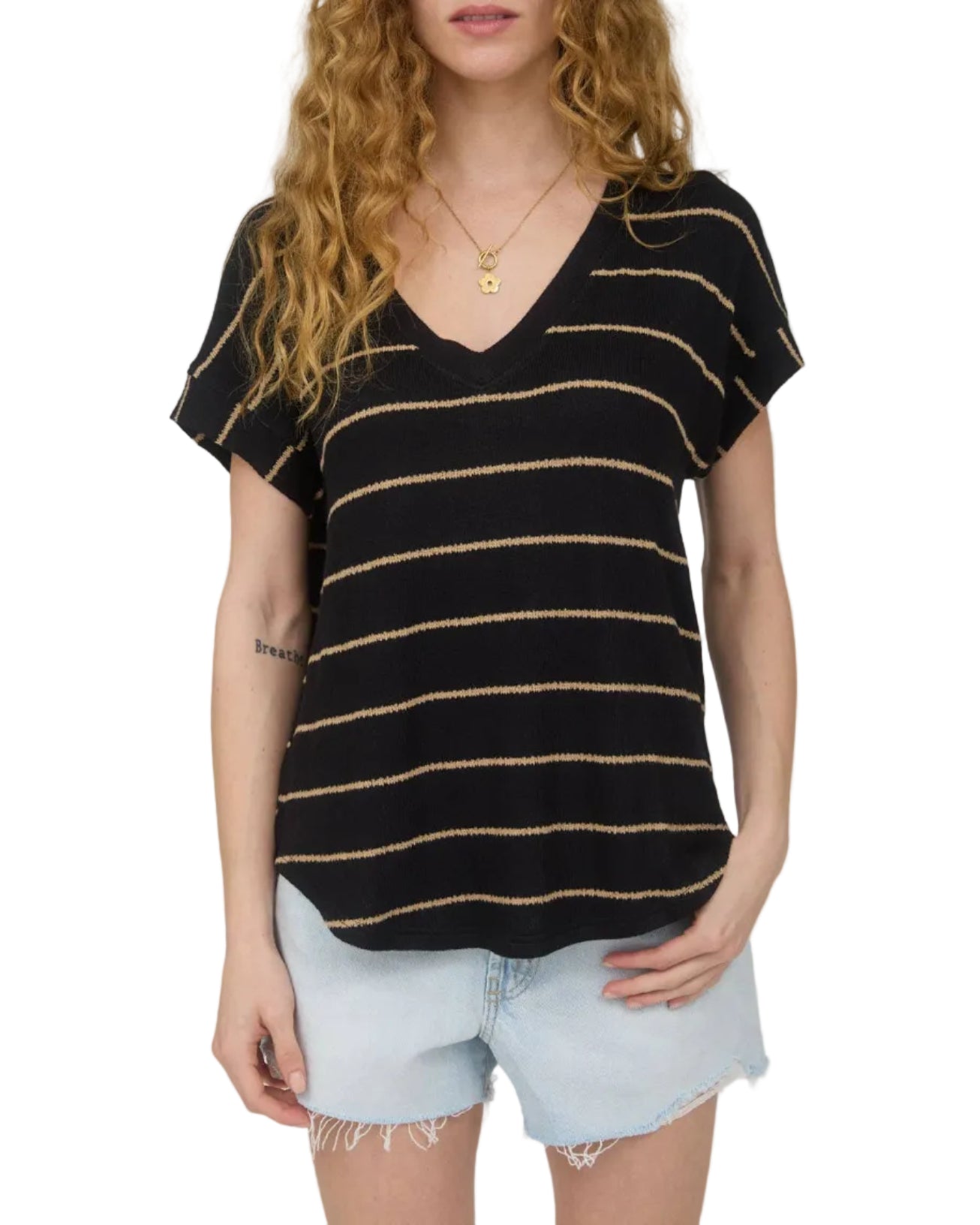 Woman wearing a black and tan striped  short sleeve shirt with light denim shorts on a plain background.