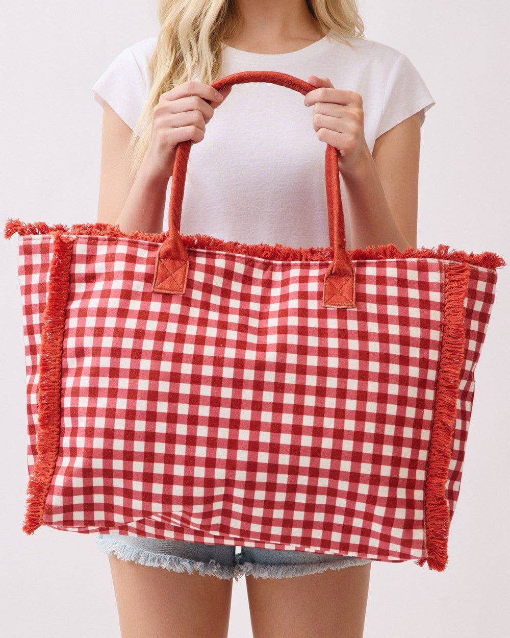 Person holding a red and white checkered bag with fringes on a plain background.