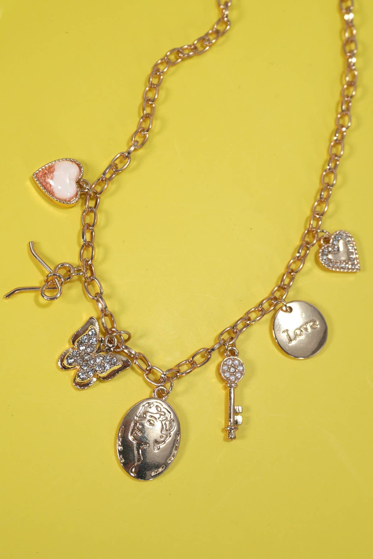 Gold charm statement necklace with a bow, heart, key, butterfly, and sparkling rhinestone accents.