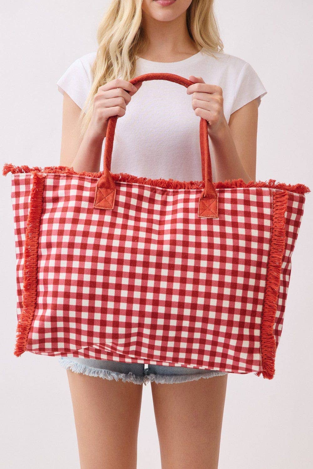 Person holding a red and white checkered bag with fringes on a plain background.