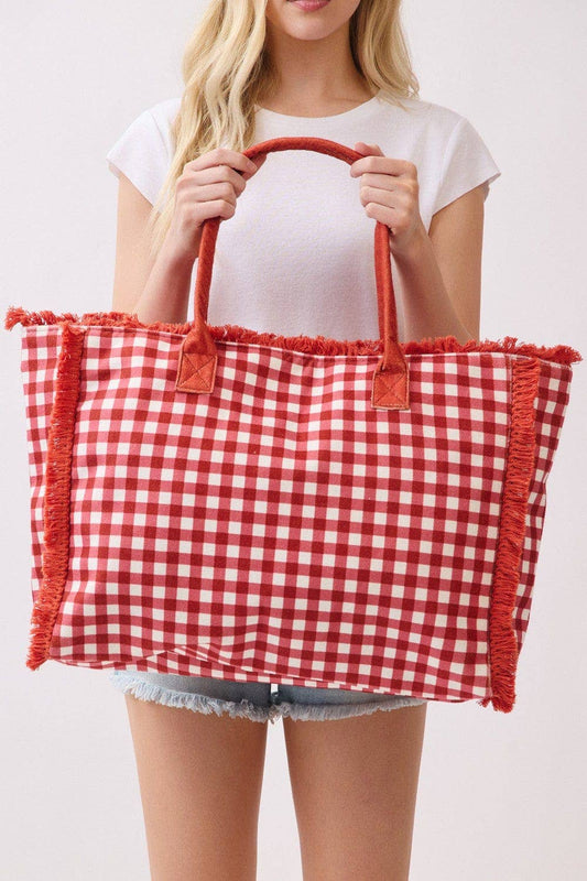 Person holding a red and white checkered bag with fringes on a plain background.