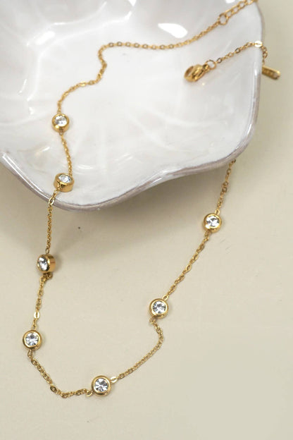 Gold necklace with rhinestones on a white dish.
