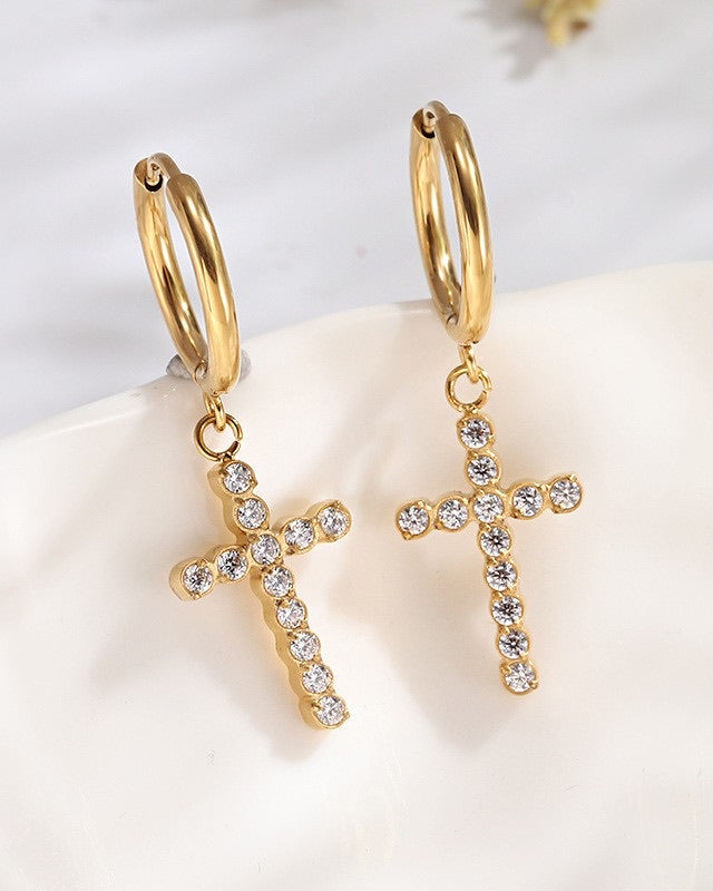 Gold hoop earrings with cross pendants and rhinestones on a white surface.