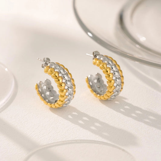 Pair of gold and silver hoop earrings with mini heart accents on a white surface.