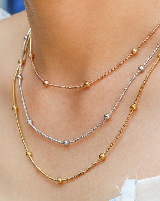Gold, Rose Gold and Silver layer necklaces with small beads on a person's neck.