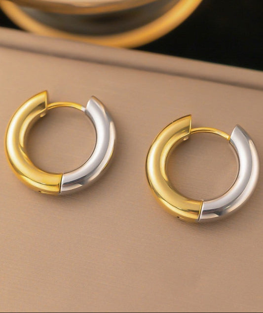 Pair of gold and silver huggie hoop earrings on a beige surface.