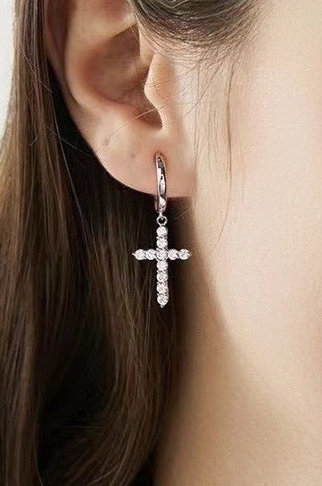 Close-up of an ear wearing a silver cross earring with rhinestones. 