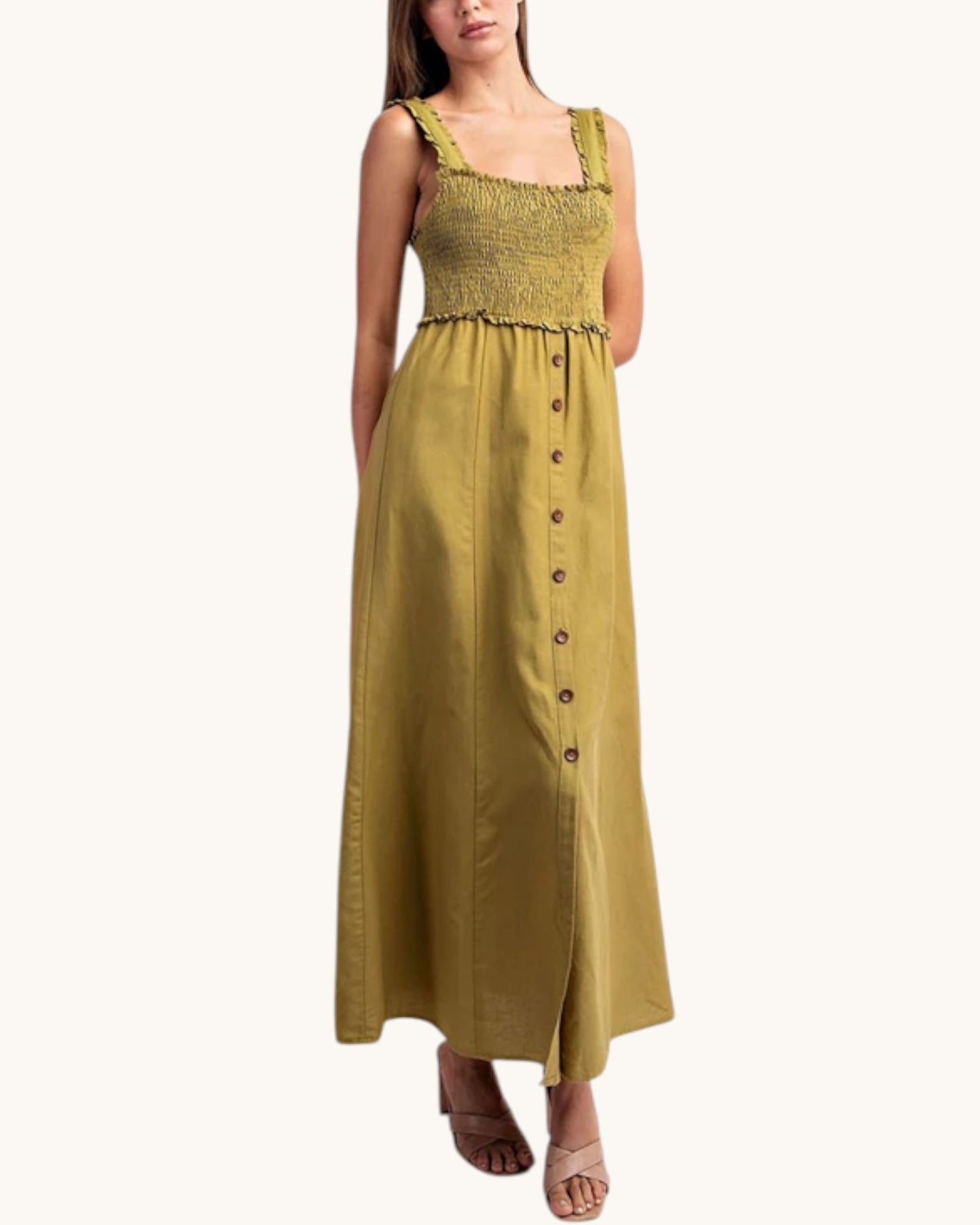 A woman modeling a sleeveless olive green maxi dress with a smocked bodice, ruffled straps, and a button-down front, set against a plain off-white background.