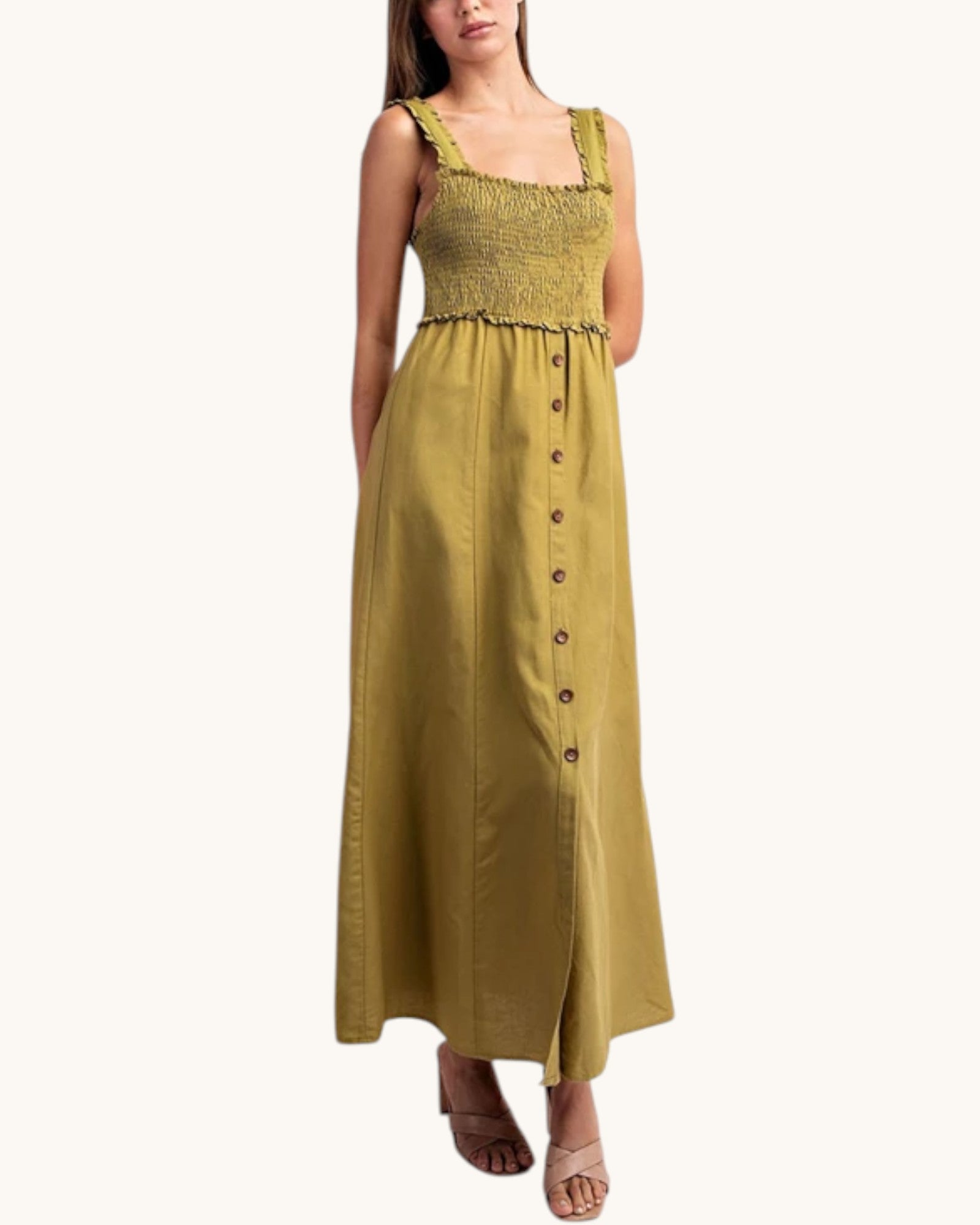 A woman modeling a sleeveless olive green maxi dress with a smocked bodice, ruffled straps, and a button-down front, set against a plain off-white background.