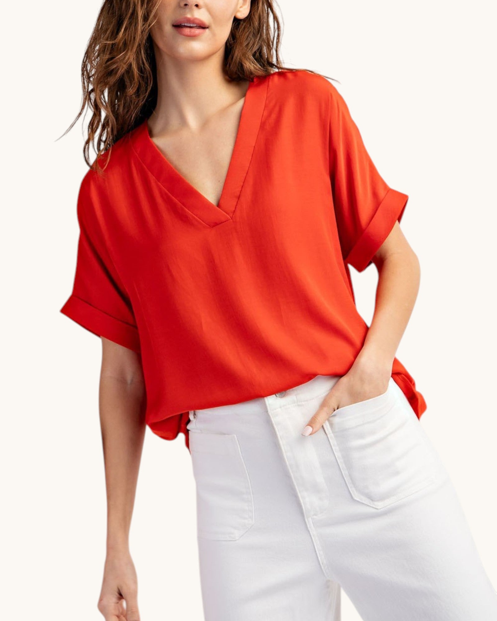 Tomato red V-neck top worn with white pants on white background, front view. 