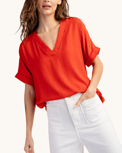 Tomato red V-neck top worn with white pants on white background, front view. 