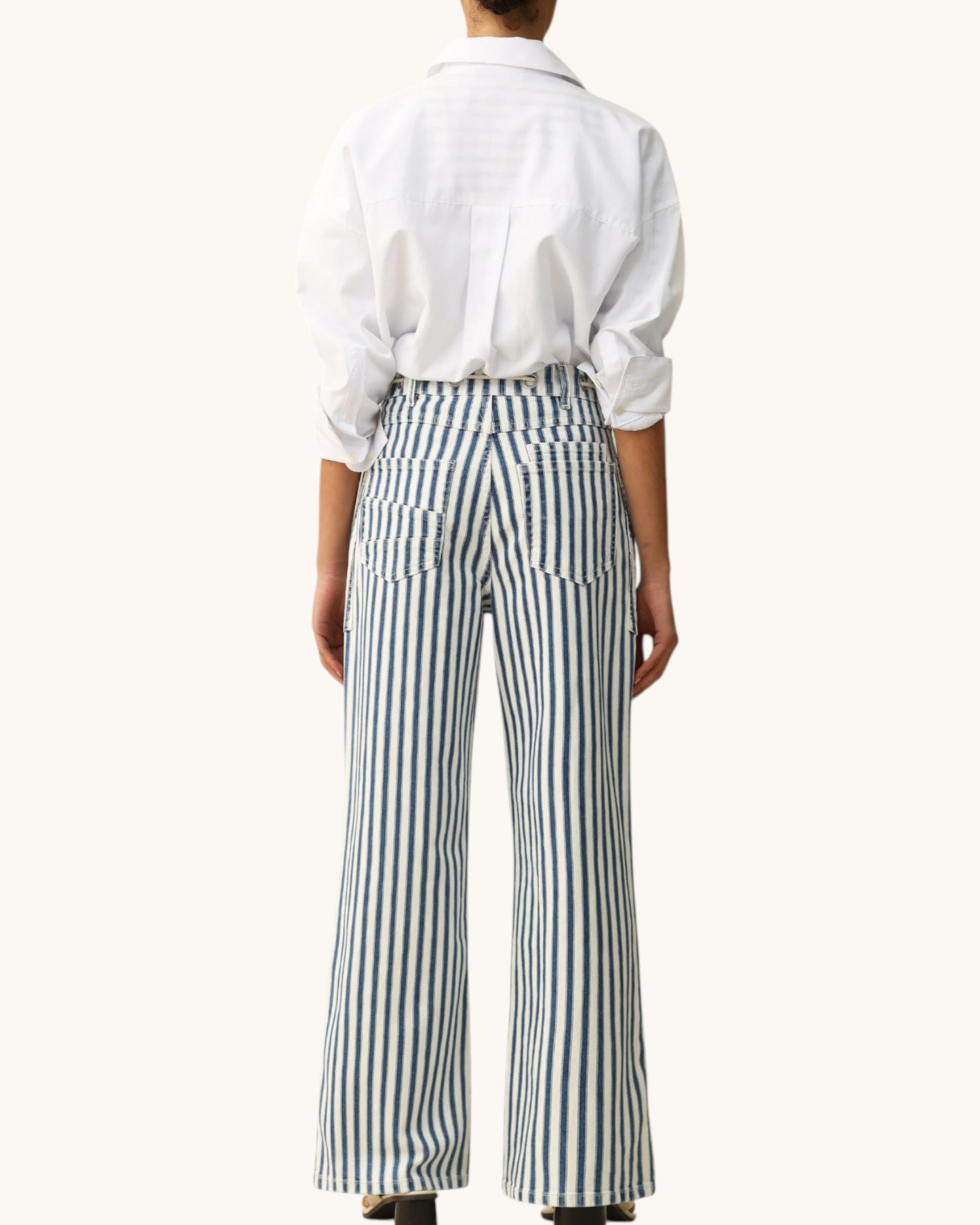 A model shown from the back wearing a white long-sleeve button-up shirt and high-waisted, wide-leg trousers with vertical navy and white stripes.