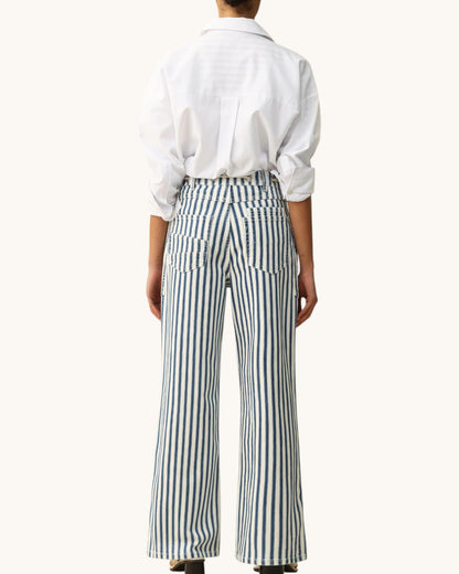 A model shown from the back wearing a white long-sleeve button-up shirt and high-waisted, wide-leg trousers with vertical navy and white stripes.