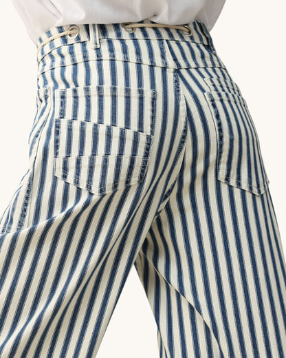 Close-up of the back waistband and pockets of striped trousers with vertical navy and cream stripes, worn with a white top against a light neutral background.