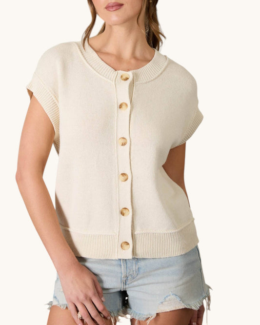 Woman wearing a cream-colored sleeveless cardigan with button details on a white background. 