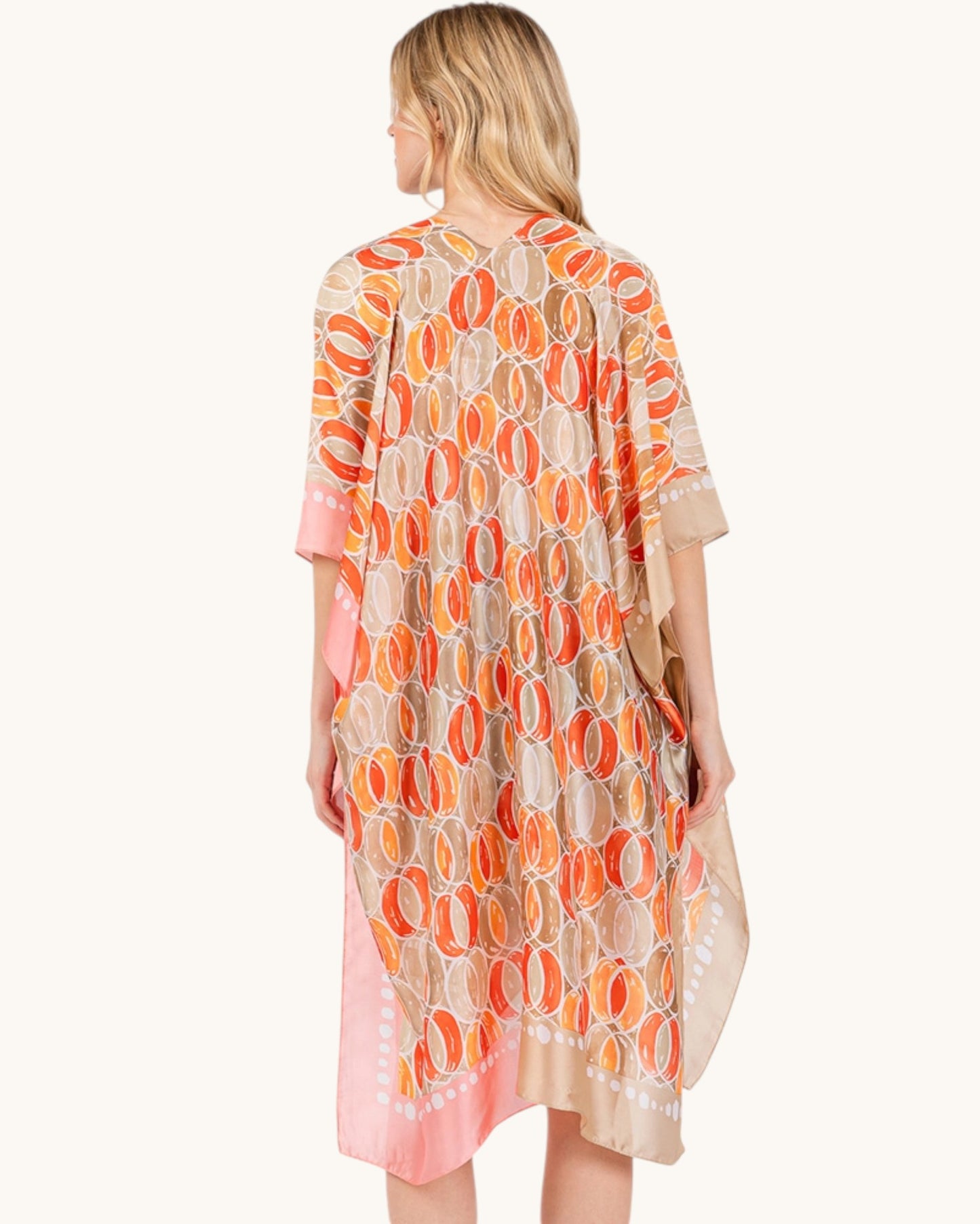 Back view of a woman wearing a patterned kimono style cover up wrap with orange and pink circles on a white background.