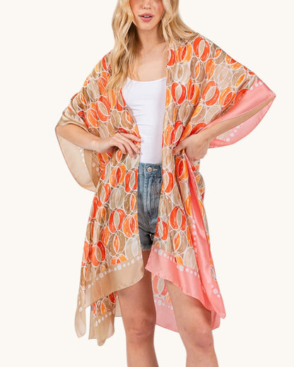 Woman wearing a colorful beige, orange and pink kimono-style cover-up on a white background.