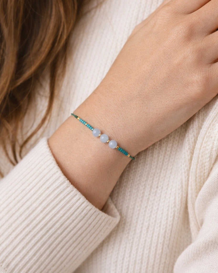 Close-up of a hand wearing a bracelet with beads on a light background.