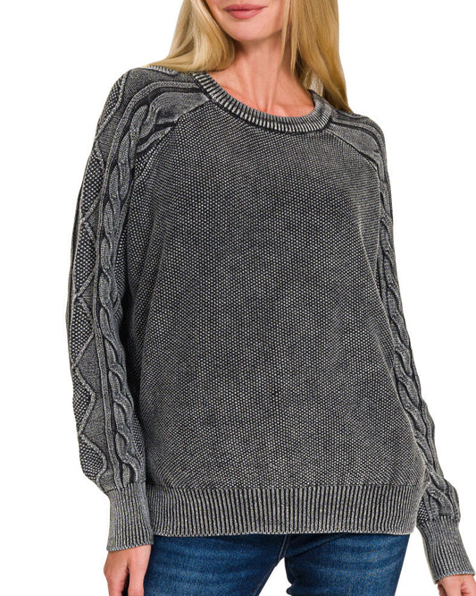 Woman wearing a charcoal cable knit sweater on a white background.