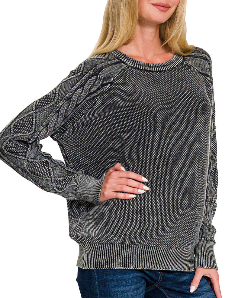 Woman wearing a charcoal sweater with cable knit design on a white background.