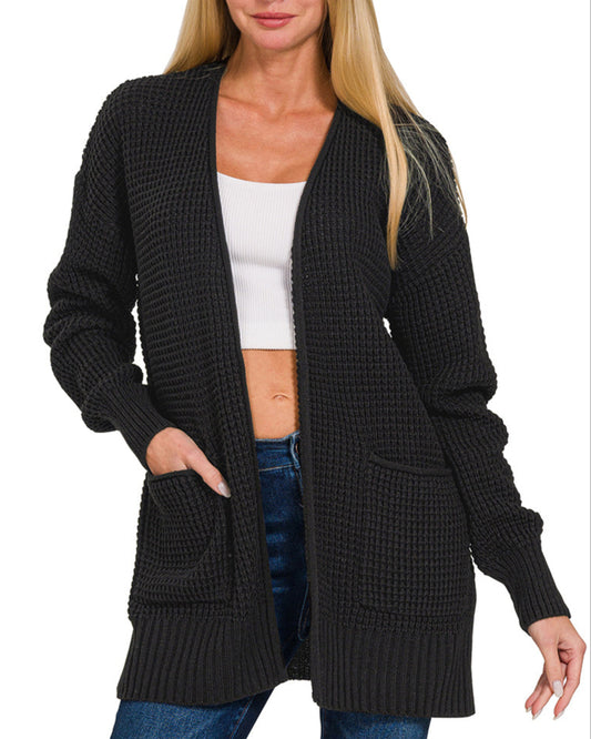 Woman wearing a black cardigan over a white top and blue jeans on a white background