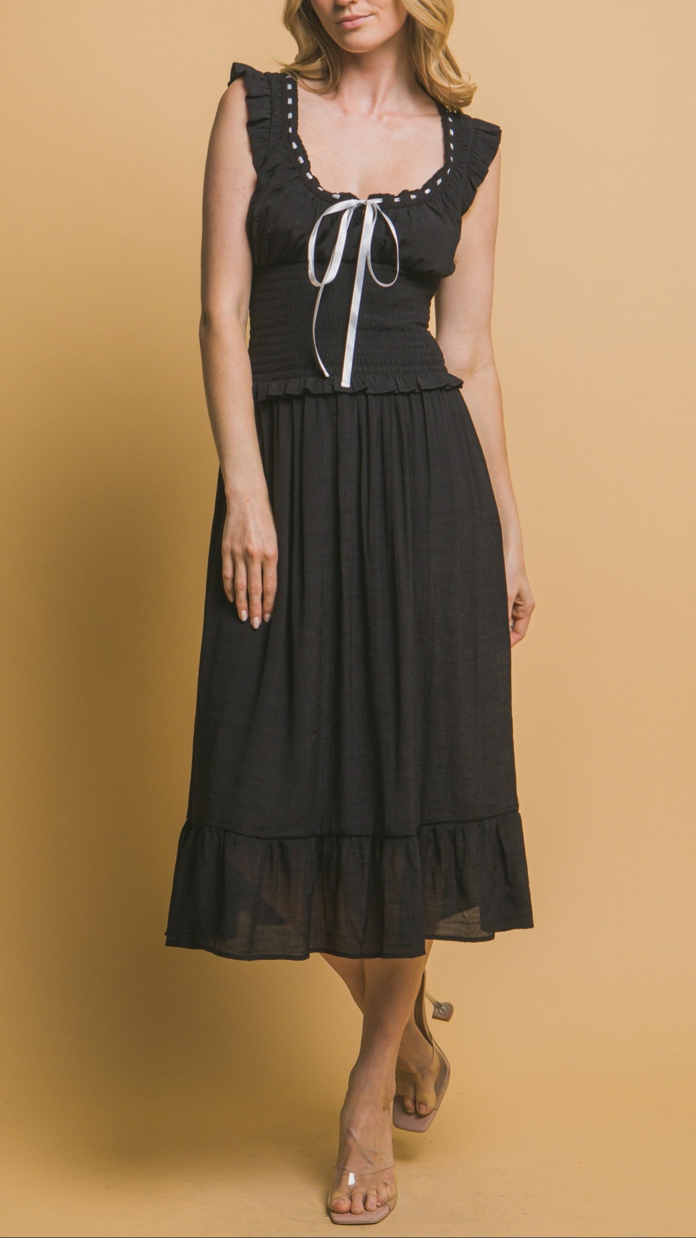 Black midi dress with white ribbon trim, smocked bodice, ruffle sleeves, and tiered hemline. Romantic and feminine style. 