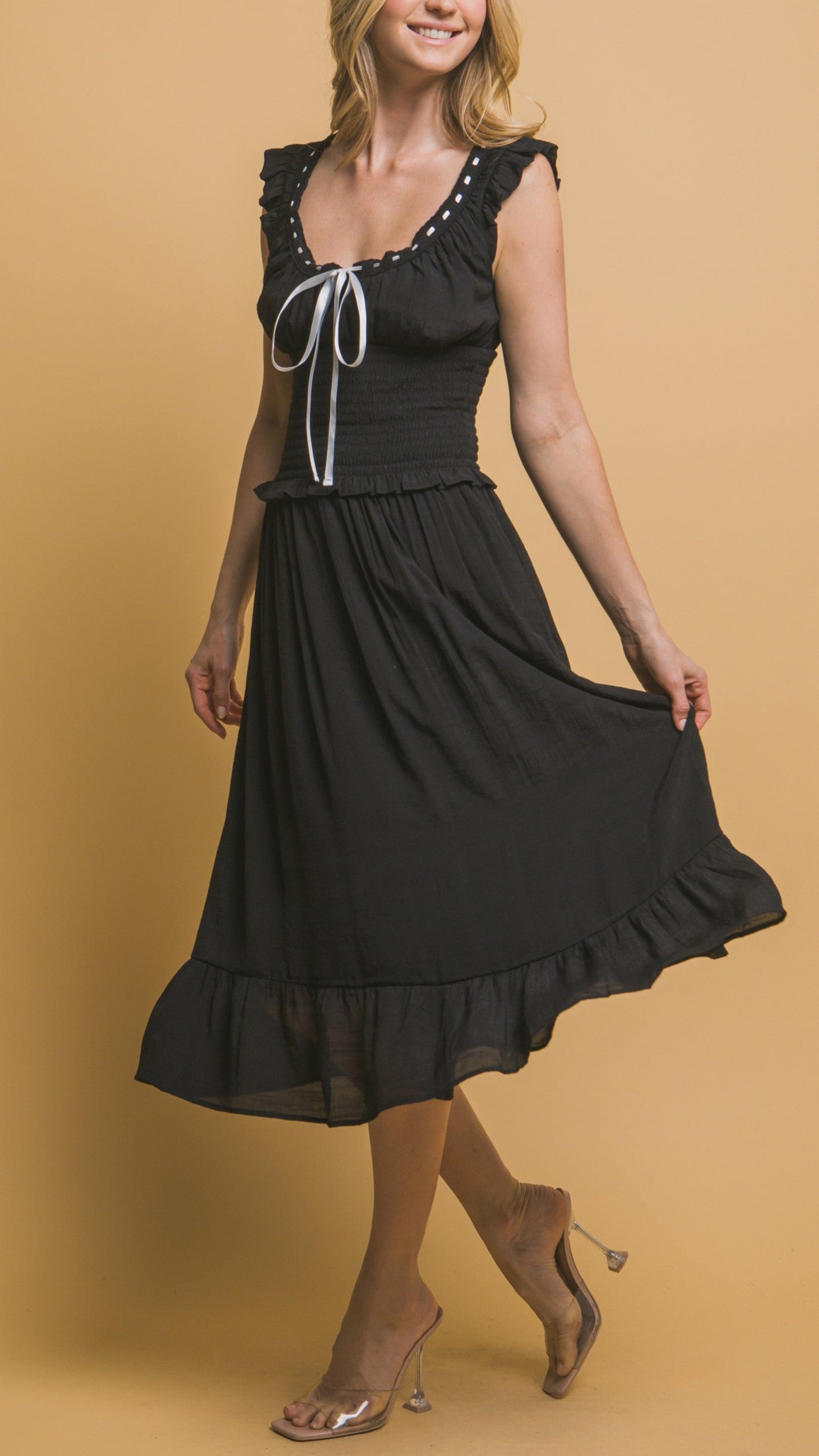 Black midi dress with white ribbon trim, smocked bodice, ruffle sleeves, and tiered hemline. Romantic and feminine style. 