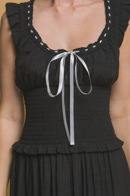 Black midi dress with white ribbon trim, smocked bodice, ruffle sleeves, and tiered hemline. Romantic and feminine style. 