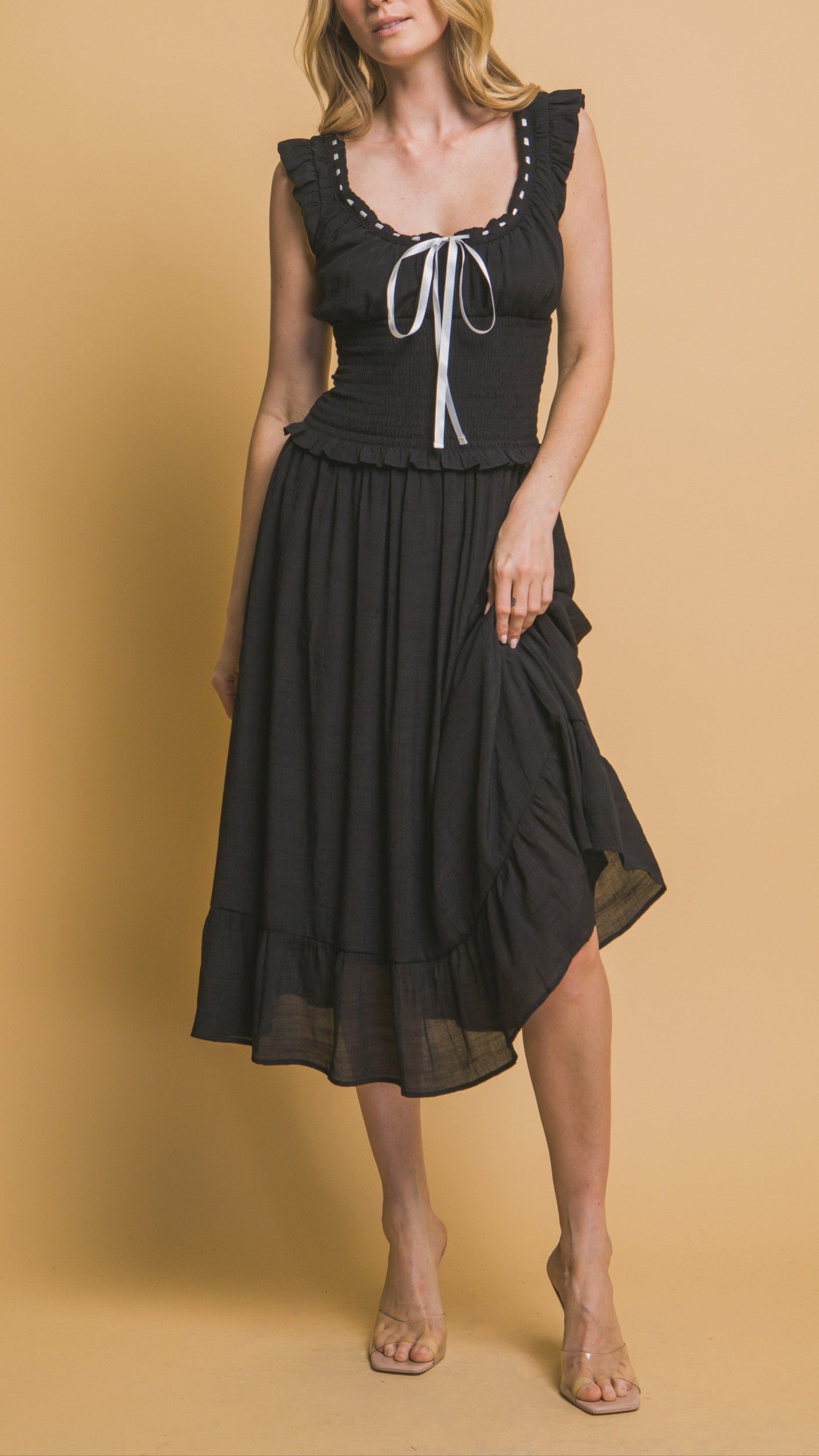Black midi dress with white ribbon trim, smocked bodice, ruffle sleeves, and tiered hemline. Romantic and feminine style. 