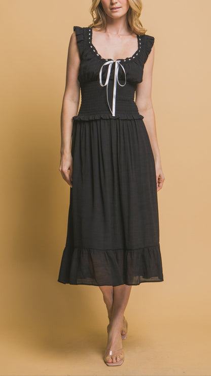 Black midi dress with white ribbon trim, smocked bodice, ruffle sleeves, and tiered hemline. Romantic and feminine style. 
